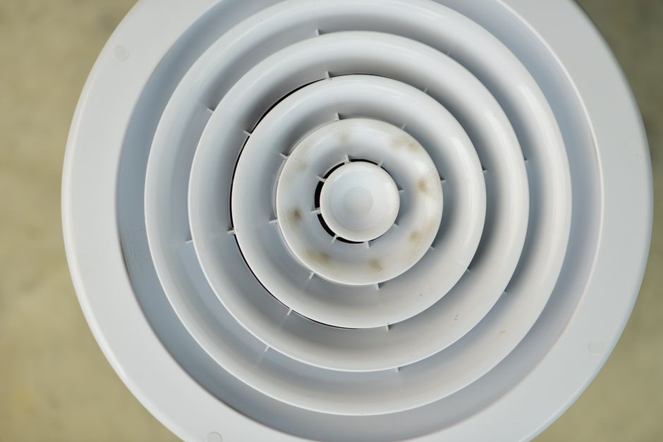 Top view of a white circular air vent highlighting its concentric design with slight discoloration.